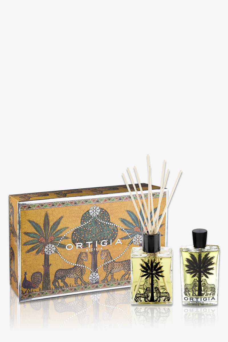 The Ortigia Casa Set includes a yellow patterned box, a glass diffuser bottle with reeds, and a matching perfume bottle, all decorated with black palm tree and animal motifs.
