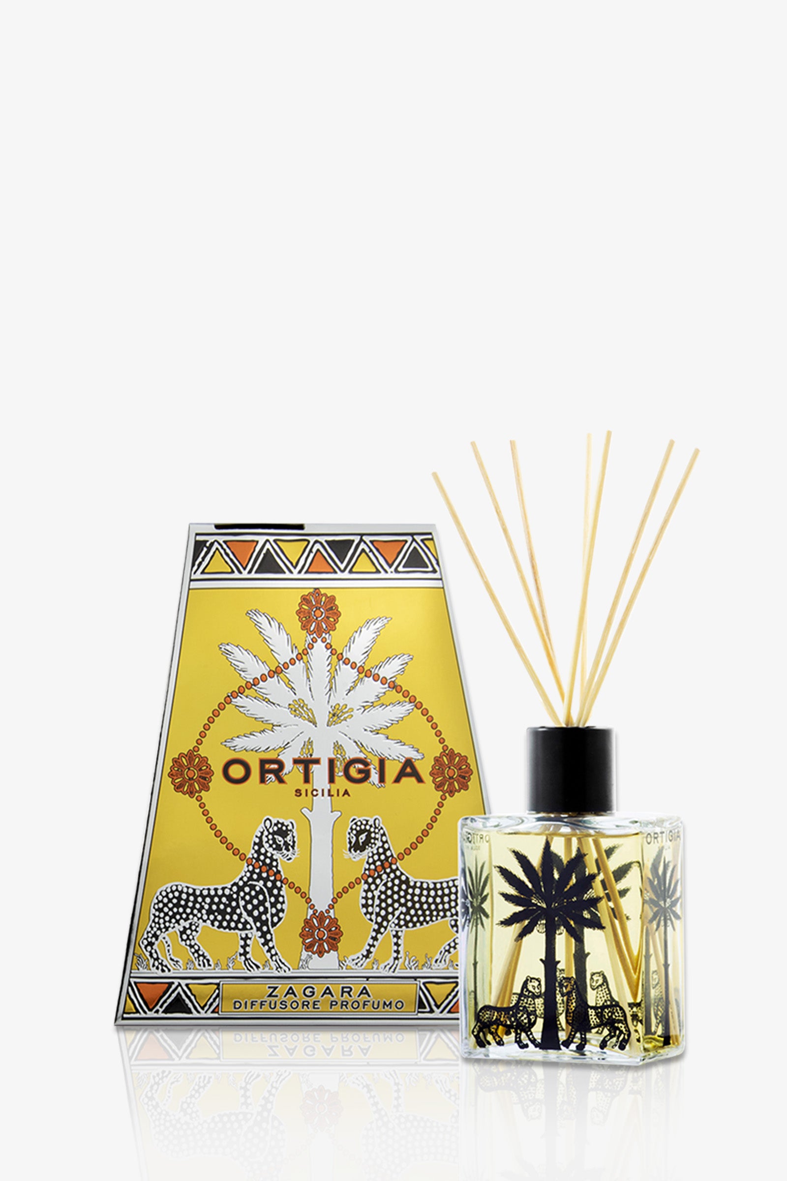 The Ortigia Diffuser features a gold box with black and white leopards, palm trees, and decorative patterns; inside is a glass bottle of scented liquid with palm tree illustrations and reed sticks.