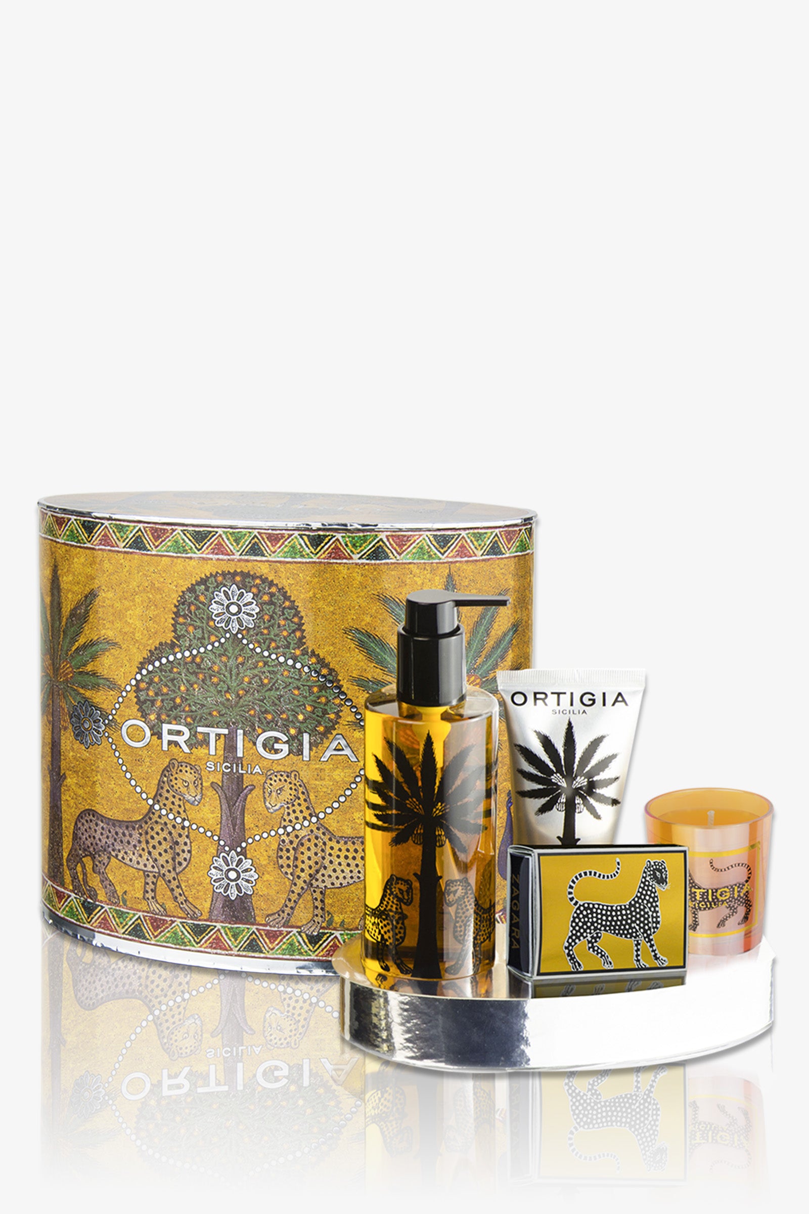 Ortigia Oval Set: a gold-patterned gift box with four items—spray bottle, tube, bar soap, and small candle—all featuring exotic animal and plant designs.