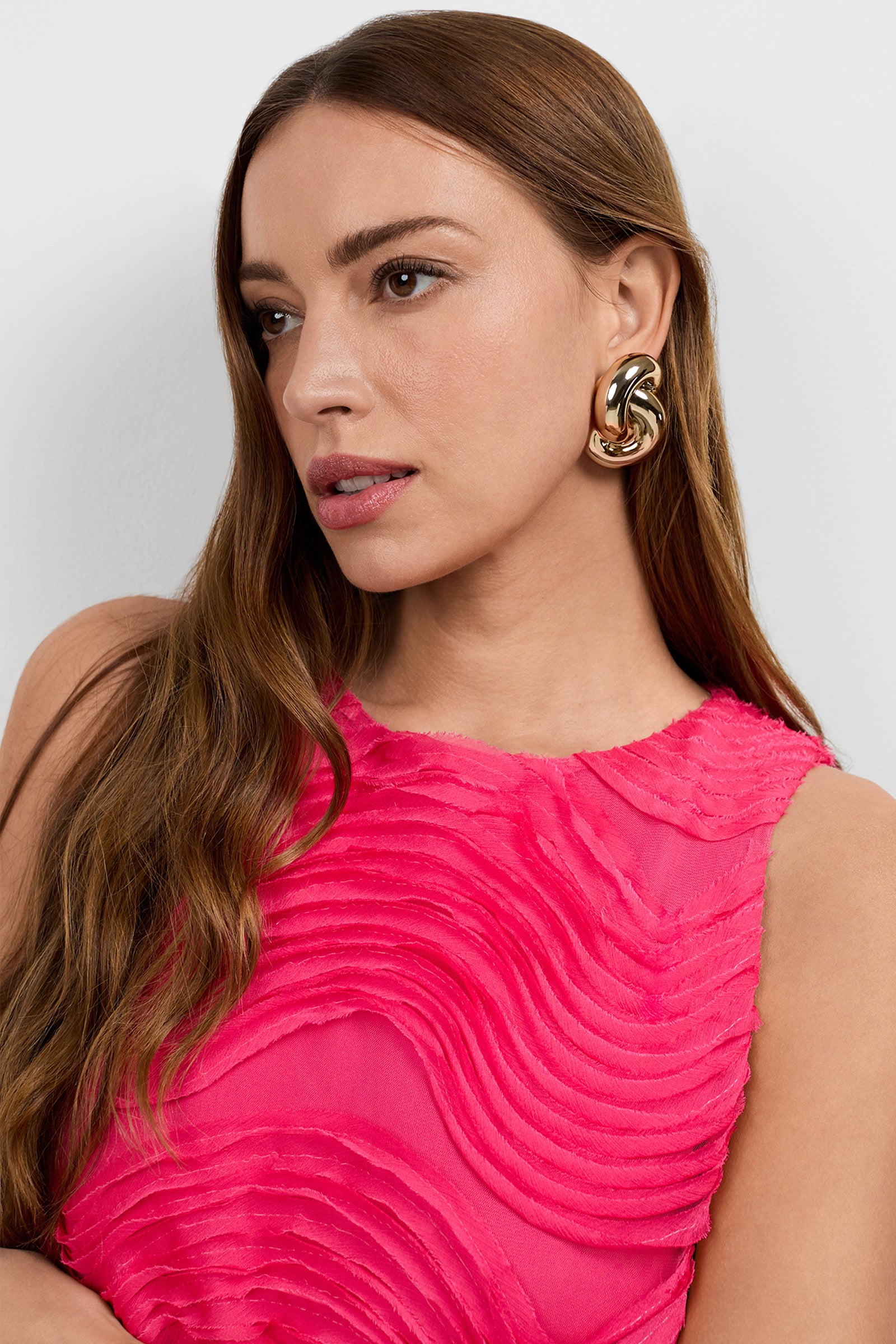 A woman with long brown hair wears chunky gold earrings and the Belisama Organza Midi Dress. She gazes slightly to the side with a neutral expression against a plain light background.