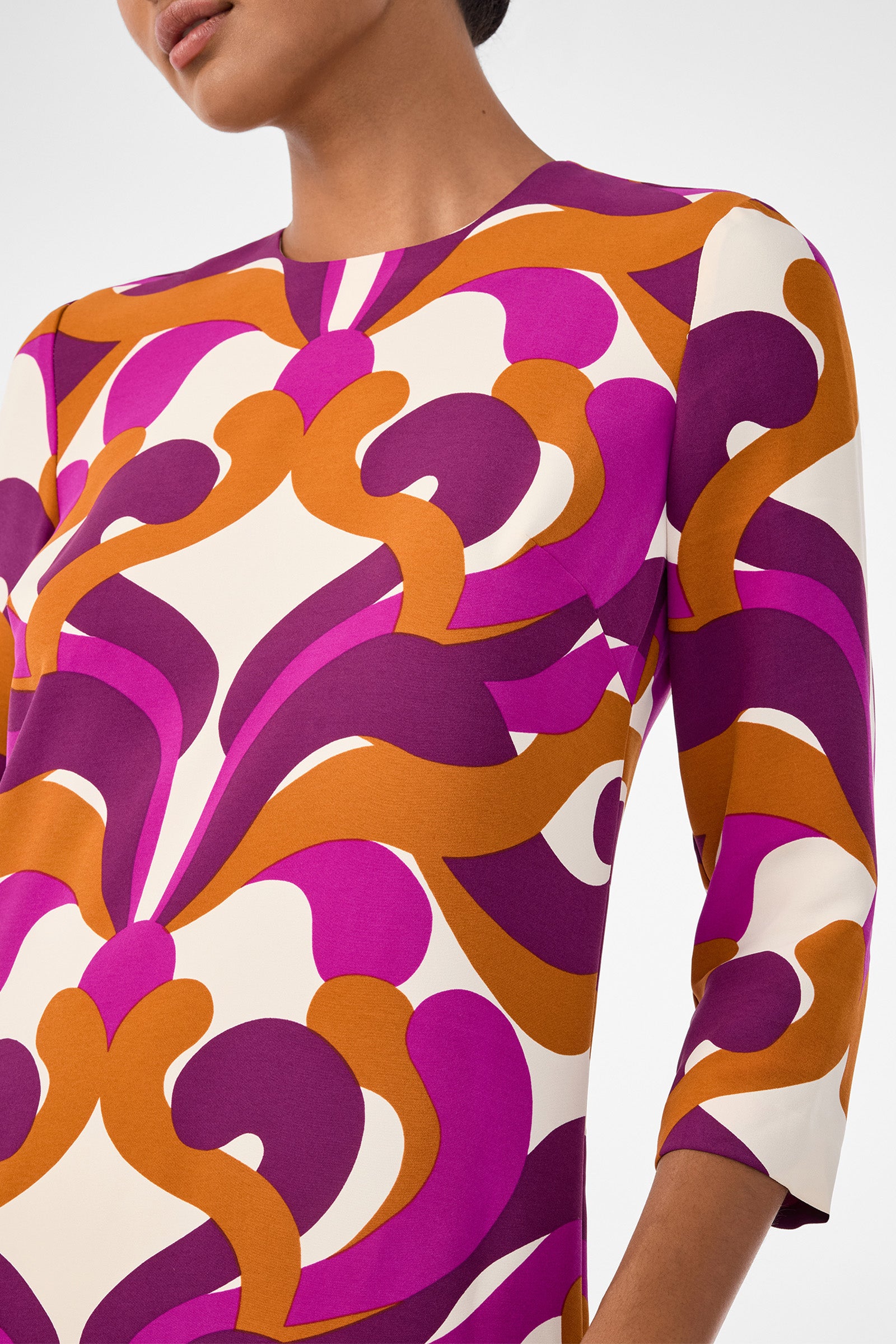 A person in the Cointreau 2 Dress, featuring bold abstract patterns in purple, magenta, orange, and white with three-quarter sleeves and a round neckline. Only the upper body is shown.