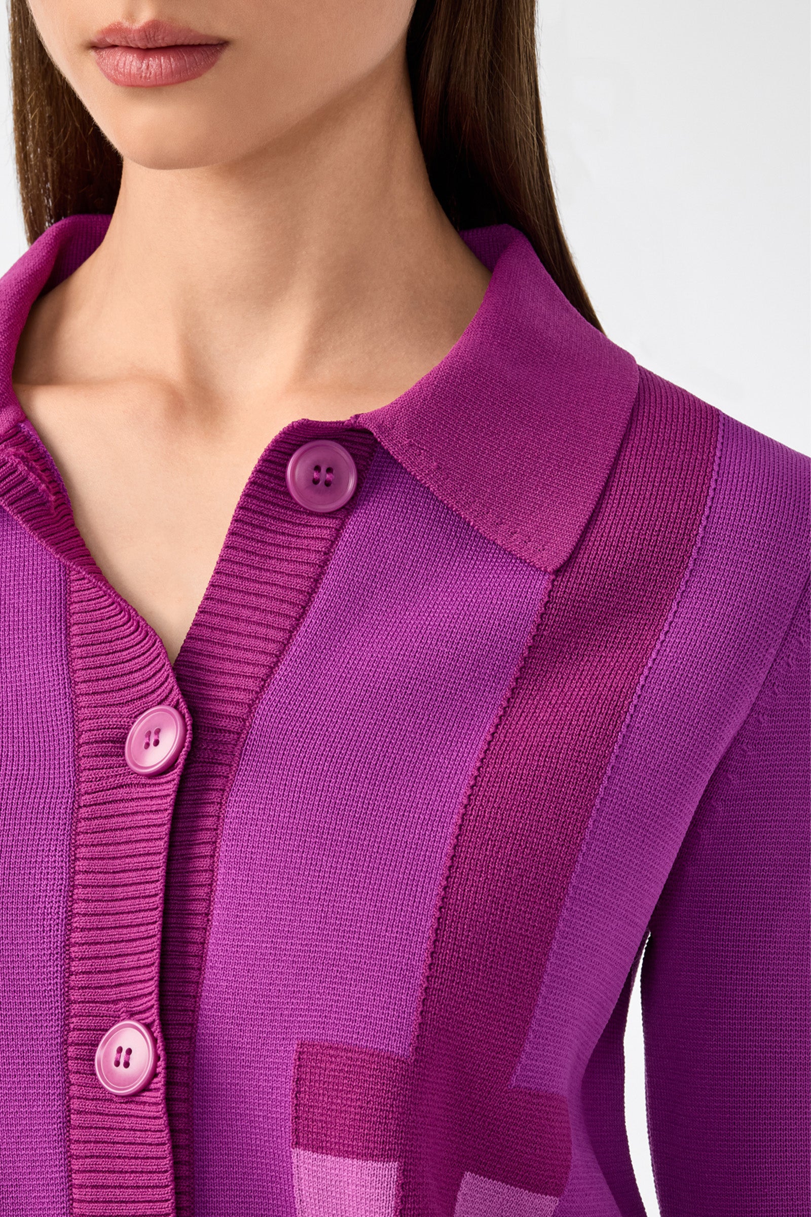 A close-up of a woman wearing the Gaia Cardigan, a bright purple button-up knit with a collar and ribbed detailing. Only her lower face, neck, and upper torso are visible.