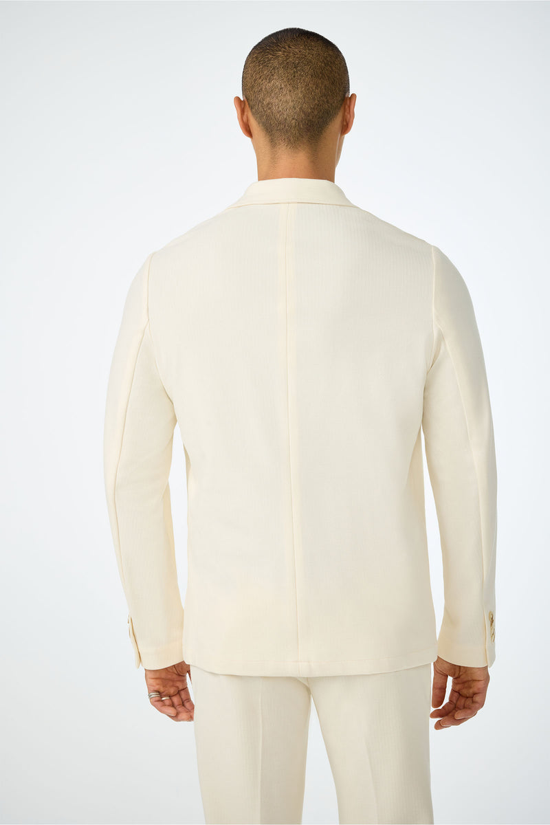 A man is seen from behind wearing the Muir Knit Blazer in cream, standing against a white background with his arms relaxed and button details visible on the jacket cuffs.