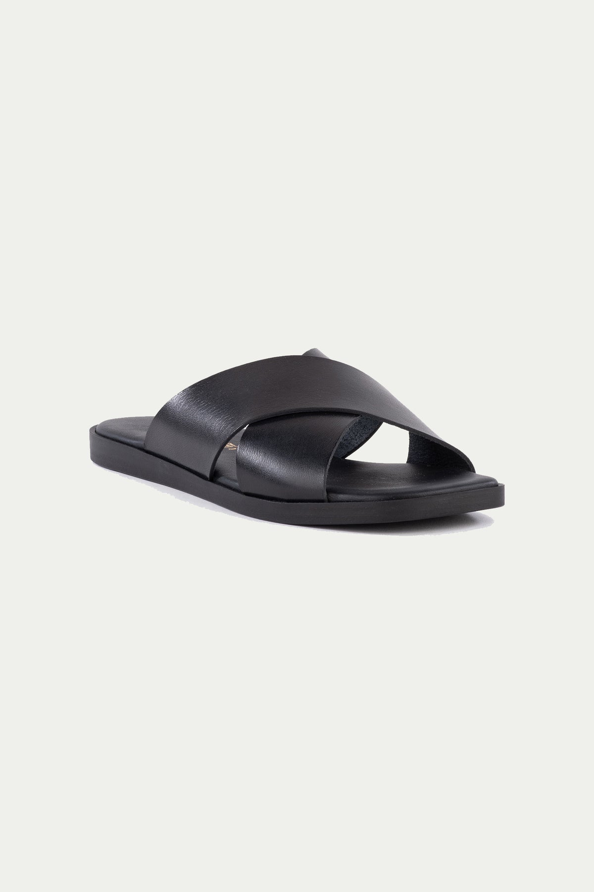 The Chai Sandal in black leather features wide crisscross straps and a flat sole, shown against a plain white background.