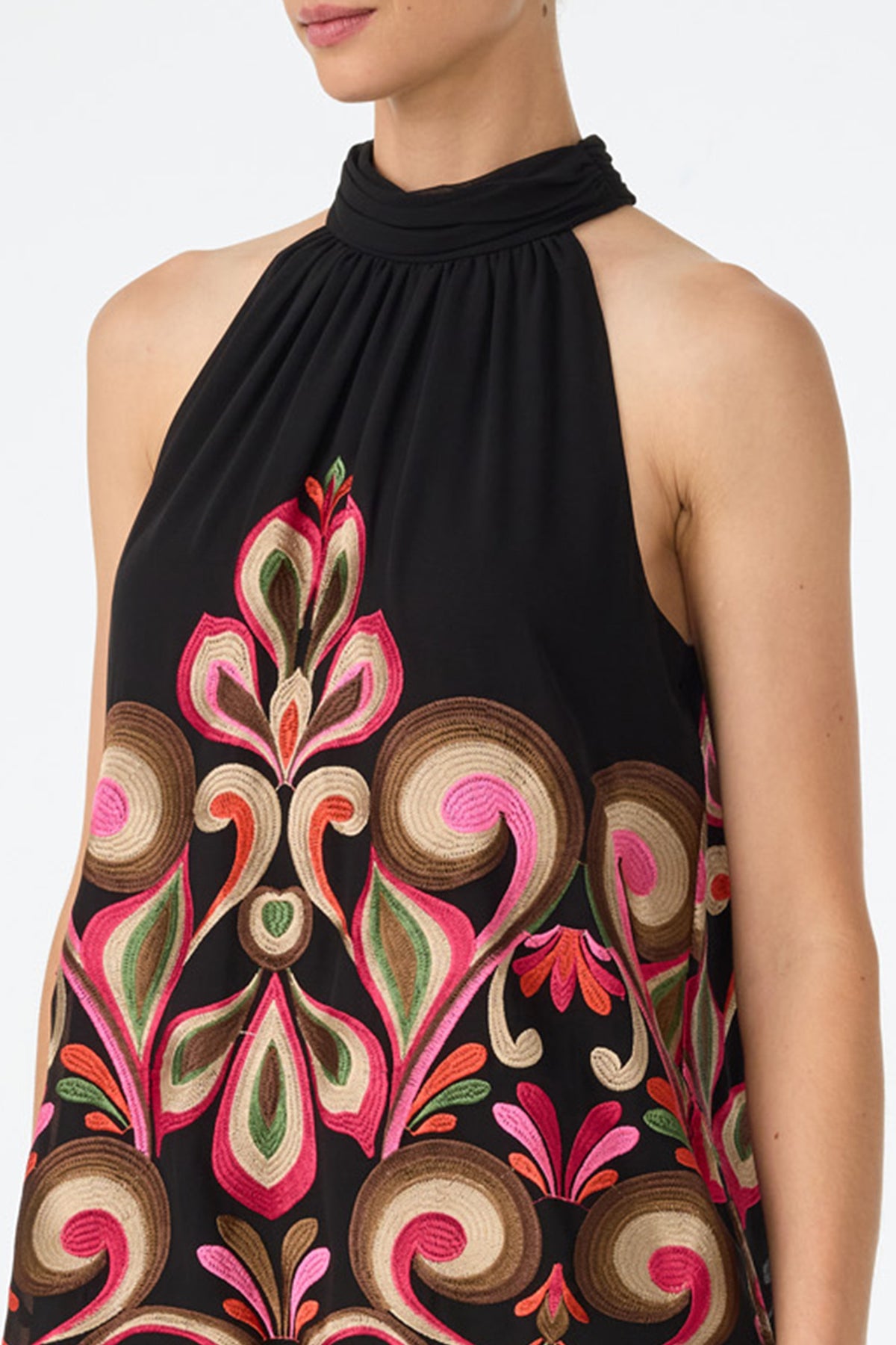 A woman wears the Zana Embroidered Mini Dress, a sleeveless black halter-neck style with intricate pink, green, brown, and gold embroidery. Her face is partially out of frame against a plain background.
