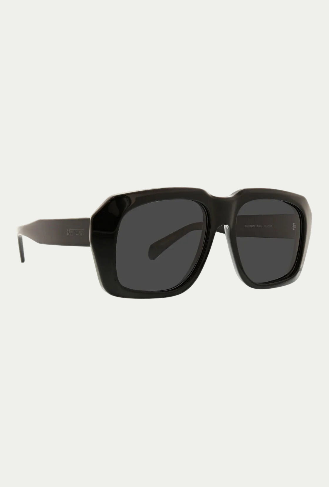 The Andros Sunglass features bold black acetate frames with thick rectangular rims and dark tinted lenses, offering 100% UVA/UVB protection, shown on a white background.