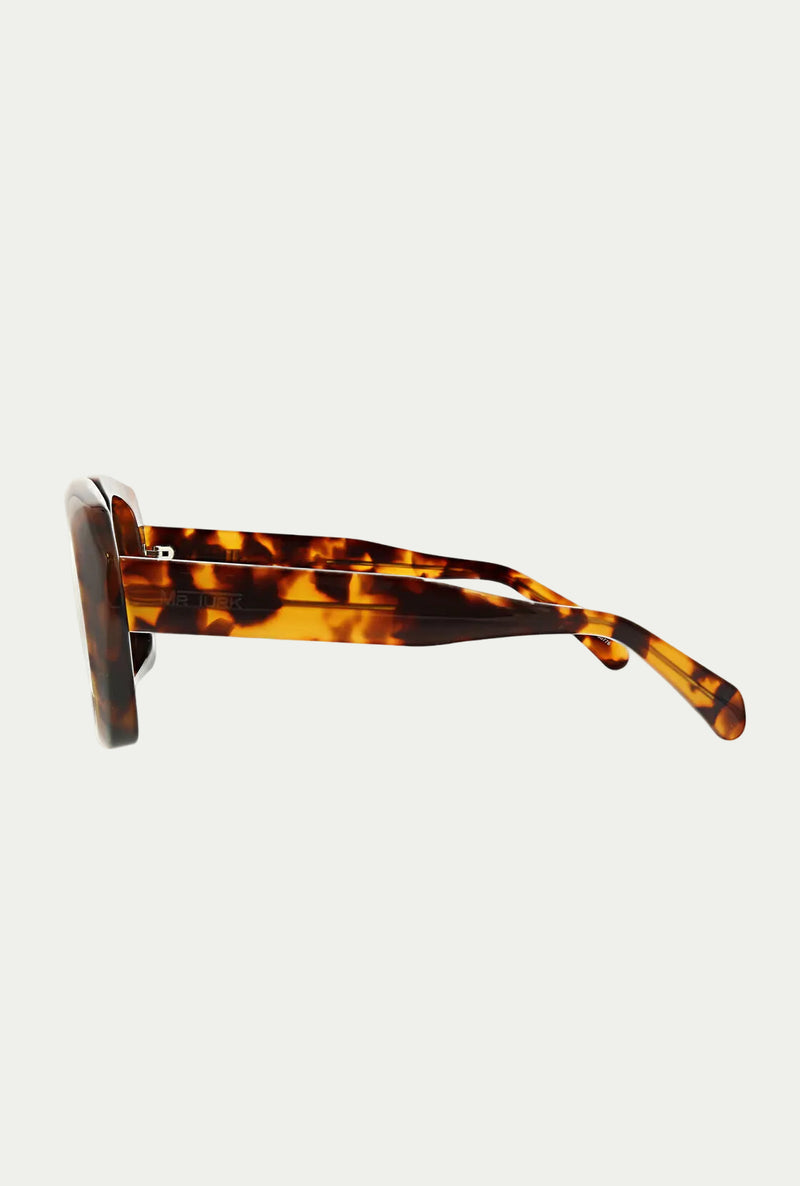 Side view of the Andros Sunglass, featuring bold acetate frames with a thick rectangular shape and brown-amber tortoiseshell arms, offering 100% UVA/UVB protection against a white background.